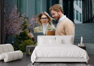 Caucasian young business partners, woman and man working during lunch break in outdoor, using laptop, discuss new project, freelancer couple Wall mural