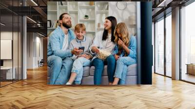 Happy woman and man with kids talking smiling laughing on sofa looking at smartphone using apps. Father daughter and son mother using smartphone application together in living room, family smartphone Wall mural