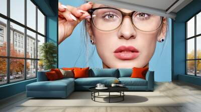 Portrait of attractive young woman in glasses on blue background Wall mural