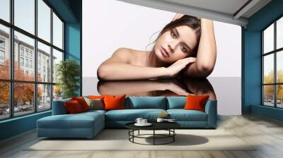 Portrait of young beautiful woman at reflecting table on gray background Wall mural