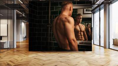 Muscular naked man looking at himself in mirror. Handsome blond guy in bathroom. Sexy shirtless fitness model near mirror. Wall mural