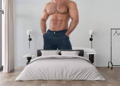 Shirtless bodybuilder in blue jeans at white background in studio Wall mural