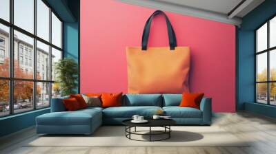 A large orange purse with a black strap sits on a pink background Wall mural