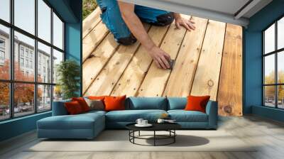 A person is kneeling on a wooden deck and sanding the boards with a sanding block. Wall mural