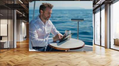 Businessman enjoying a cup of coffee while reading news on tablet on a yacht at sea Wall mural