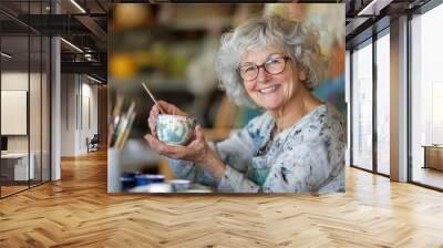 Joyful senior woman engaged in painting a cup at her studio as a retirement hobby and small business Wall mural