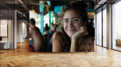 Portrait of woman in glasses smiling at camera with natural light in coffee shop setting Wall mural