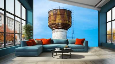 White with yellow brown color rusted old water tower on the background of a bright blue spring sky. With cornice and stairs. Wall mural