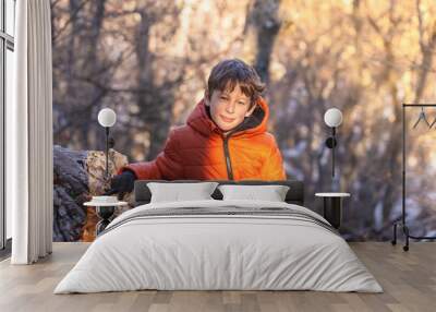 A boy standing by a stone in the mountains in the forest squints from the bright winter sun. Portrait of a boy from the waist up (8 years old, white, Caucasian) in the mountains in winter Wall mural