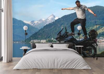 Biker man stand on top of a motorcycle keeps balance, extreme. hobby concept, adventure on two wheels. Sunny summer day in the Alpine mountains. Zell am see lake on background Austria. Copy space Wall mural