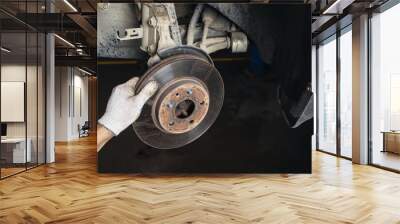 An auto mechanic is engaged in the maintenance of a passenger car in a car workshop, removes an old brake disc to replace it with a new one Wall mural