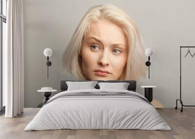 middle aged blonde woman moving brow skeptically looking aside, isolated on gray background Wall mural