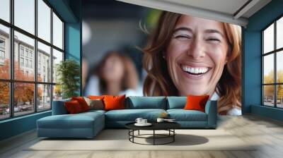 Close-up of a cheerful woman smiling brightly with blurred people in the background, capturing a joyful and positive moment. Wall mural