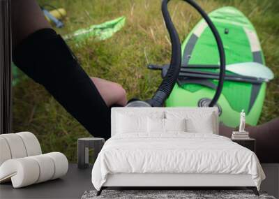 Girl hand close up inflating stand up paddle sup board with manual pump at green grass background. repeat pressure gauge with vise. Selective focus. Wall mural