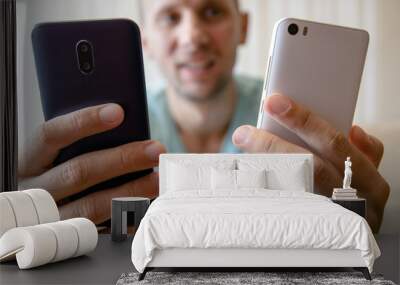 guy with two smartphones in his hands with a smile looks at the screen Wall mural