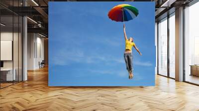 flying girl with colorful umbrella in the blue blue sky Wall mural