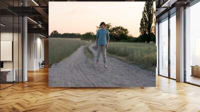 A barefoot teenager in comfortable clothes stands on a dirt road. Wall mural