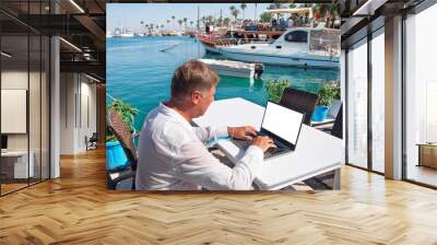 Man with laptop  on the beach is working. Social distancing in quarantine, networking, work online, creative profession. Freelancer using a laptop. Restaurant terrace, restrictions due to coronavirus. Wall mural