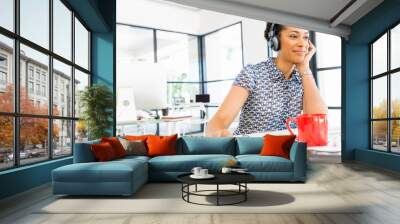 Portrait of smiling afro-american office worker sitting in offfice with headphones Wall mural