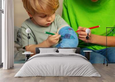 Boy and brother draw broken hand plaster cast using felt-tip pen Wall mural