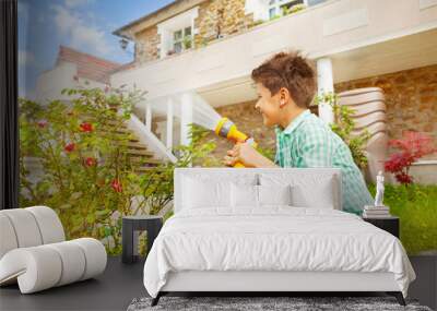 Boy watering rosebushes in the garden at sunny day Wall mural