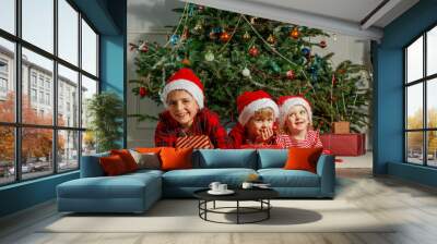 Boys and girl in Santa hat lying under decorated Christmas tree Wall mural