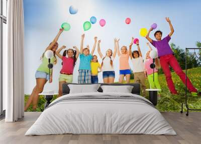 Children standing with arms up to flying balloons Wall mural