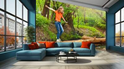 Cute girl balancing while crossing a log bridge Wall mural