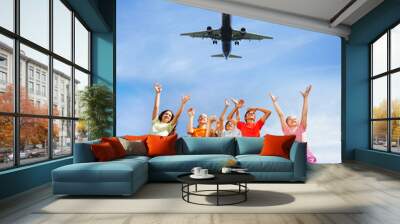 Excited children with hands up to plane in sky Wall mural