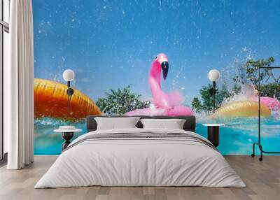 Funny action photo in the outdoor swimming pool with splashes of inflatable flamingo and doughnuts buoys rings Wall mural