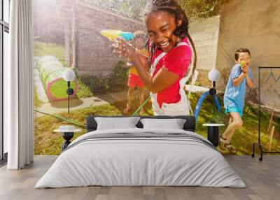 Girl with group of kids play water pistol fight Wall mural