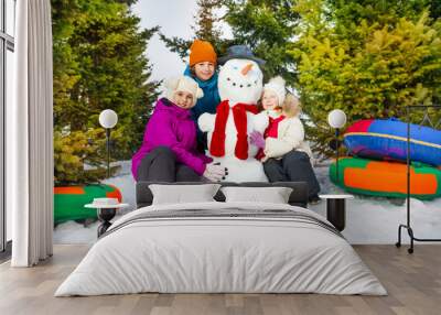 Happy children sitting close to cheerful snowman Wall mural