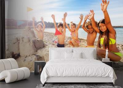 Happy friends sitting on beach around sandcastle Wall mural