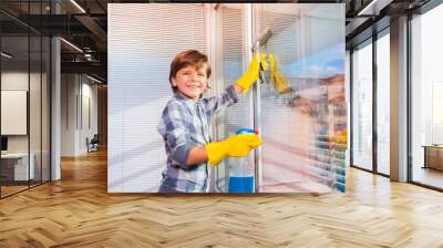 Smiling boy washing windows with window cleaner Wall mural