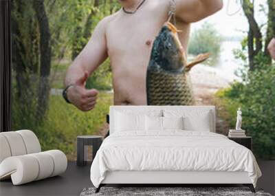 The fisherman holds in his hands a large fish caught. Good catch. Vertical photo, a hot summer day. Wall mural