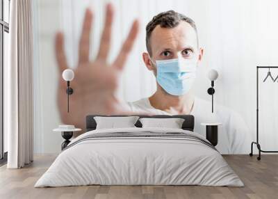 young man in medical mask shows open palm stop gesture on light background Wall mural