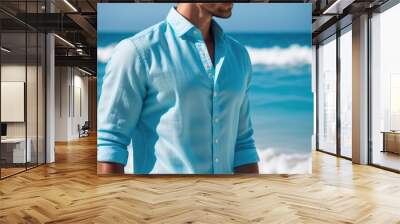 Young man standing on the beach wearing blue linen shirt with an ocean in the background Wall mural