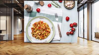 delicious vegetable stew in a white plate with a fork, with spices, garlic and tomatoes on a branch, on a napkin on blue wooden rustic background top view Wall mural