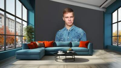 Portrait of young handsome man in jeans shirt looking at camera over dark grey background. Emotions and facial expressions concept. Wall mural