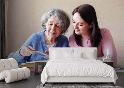 Grandmother and daughter watching a family album with old photos together - Linking generations in a common activity - An elderly and a young woman talking together-Family relations concept Wall mural