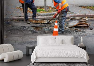 A team of road workers with a shovel and iron crowbar is repairing a sewer hatch on the roadway. Wall mural