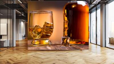 Beautiful whiskey bottle and glass of whiskey with ice on a textured dark wooden background with. Close up. Wall mural