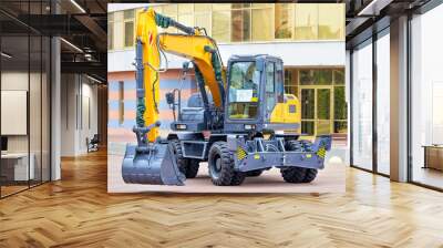 New wheeled construction excavator against the backdrop of a building on a sunny day. Wall mural