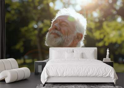 A senior man with white hair and a beard is practicing deep breathing exercises in a park on a sunny day. He is wearing a white sleeveless shirt and his eyes are closed as he inhales deeply Wall mural