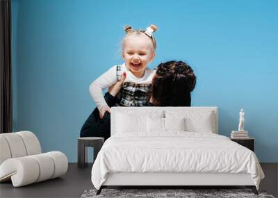 Happy laughing little girl daughter in her mother's arms against the blue sky Wall mural