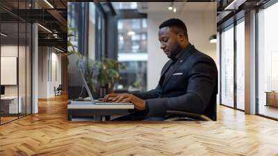 Professional black man in wheelchair working on laptop in modern office environment, focused and determined Wall mural