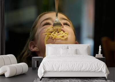 teenage girl eating spaghetti with her mouth open upwards as the spaghetti falls from the fork into her mo Wall mural