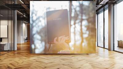 Raised hand holding the Holy Bible illuminated by morning sunlight. copy space. Horizontal shot. Wall mural