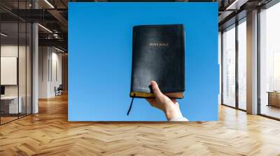 Raised hand holding the Holy Bible. Background with blue sky on a beautiful winter morning. Copy space. Close-up. Horizontal shot. Wall mural