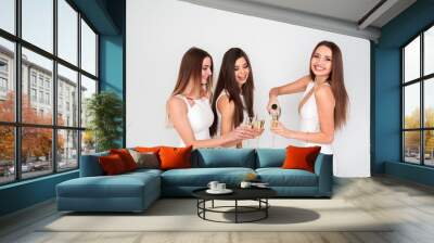 Three young woman in elegant dresses having fun, smiling, dancing and drinking champagne in studio on white background. Christmas party celebration concept. Wall mural